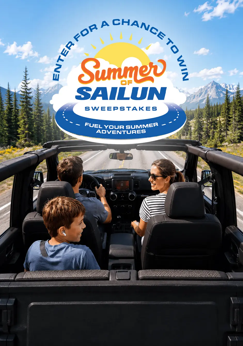 A family rides in an open-top SUV along a scenic mountain road lined with pine trees, with a lake and snow-capped peaks in the background. A large “Summer of Sailun Sweepstakes” graphic is overlaid in the center, with text above reading “Enter for a chance to win” and a tagline below, “Fuel your summer adventures.”