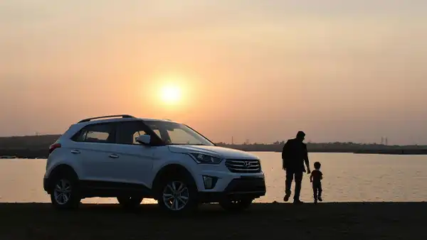 White SUV parked beside a lake at sunset with an adult and child standing near the water.