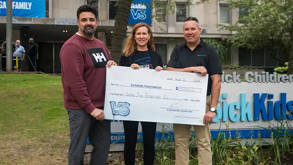 Three people holding a Sailun Tire donation cheque in front of the SickKids Hospital sign.