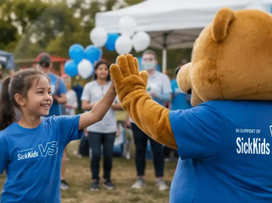 Young participant high-fiving a mascot at a SickKids community fundraising event supporting the “A Helping Hand” initiative for families in need.