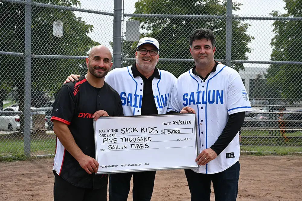 Group photo at a charity softball event, with participants holding a donation cheque.